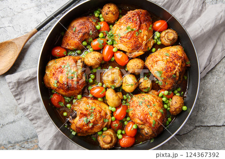 Honey garlic chicken thighs baked with mushrooms, green peas, cherry tomatoes and herbs close-up in a frying pan. Horizontal top view 124367392