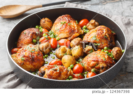 Honey garlic chicken thighs baked with mushrooms, green peas, cherry tomatoes and herbs close-up in a frying pan. Horizontal 124367398