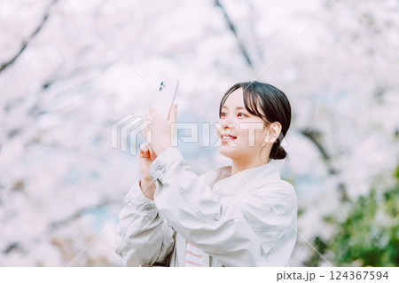 桜並木をスマホで撮影する若い女性 124367594