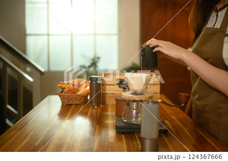 Close up of woman pouring hot water into a coffee dripper on a wooden kitchen counter Close up of woman pouring hot water into a coffee dripper on a wooden kitchen counter 124367666