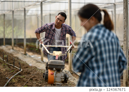 Male farmer works with a cultivator machine to prepare the soil in a greenhouse 124367671