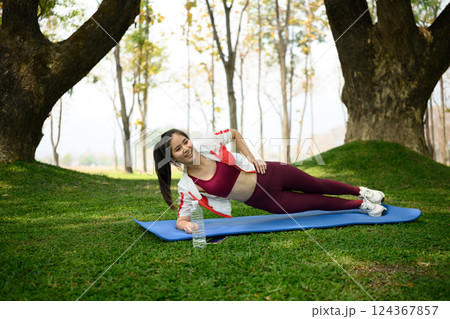 Sporty young woman doing side plank on yoga mat in the park 124367857