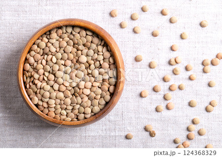 Large green lentils in a wooden bowl on linen fabric. Unshelled, dried plate lentils, a typically larger, flat variety of lentils, that hold their shape when cooked, used in soups, stews, or salads. 124368329