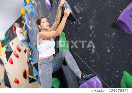 Young girl moving on bouldering wall at indoor climbing gym Young girl moving on bouldering wall at indoor climbing gym 124370572