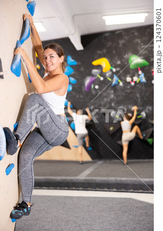 Young woman climbs steep artificial wall in sports complex and trains endurance 124370601