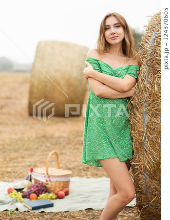 Young seductive sexy girl in summer green dress posing near stack of straw enjoying holidays in countryside in field 124370605