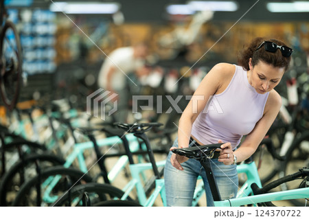 Attentive woman examining quality seat and choosing bike in bicycle sports store Attentive woman examining quality seat and choosing bike in bicycle sports store 124370722