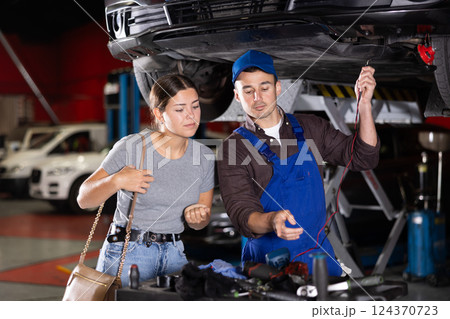 Guy mechanic checking woman client's car with measuring device Guy mechanic checking woman client's car with measuring device 124370723