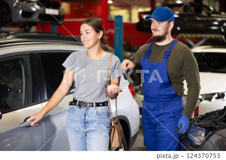 Kind car mechanic handing over the keys of car to glad female client in auto shop 124370753