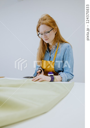 female seamstress cuts product from a roll of fabric in sewing workshop. fashion industry. 124370833