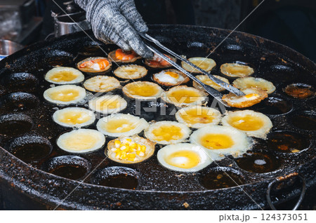 cooking a traditional Vietnamese dish Banh Khot with shrimps and corn at Asian night market on the street in Vietnam in Asia 124373051