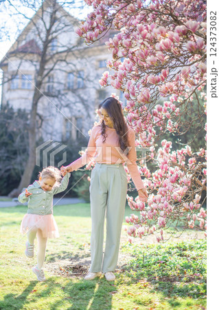 Young mother with her little daughter in a blooming magnolia garden in Prague. Symbol of maternal love and the beauty of springtime bonding in nature 124373082