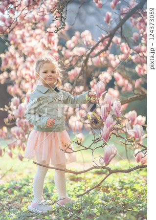 Adorable little girl standing under blooming magnolia trees in a Prague park. A sweet childhood moment filled with curiosity and spring vibes. 124373089