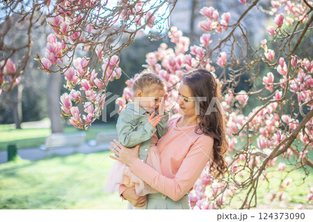 Trendy mom with her little daughter under blooming magnolia trees in a Prague park. Capturing a stylish family moment with a modern approach to parenting Trendy mom with her little daughter under blooming magnolia trees in a Prague park. Capturing a stylish family moment with a modern approach to parenting 124373090