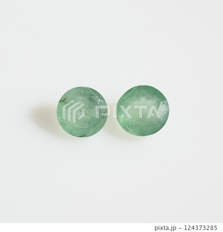 Close-up of Two Faceted Natural Emerald Gemstones Against a Clean White Background, Showcasing Their Green Hue and Internal Inclusions 124373285