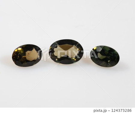 Three Natural Faceted Oval Kornerupine Gemstones Displaying Olive Green and Yellowish Brown Colors on White Background 124373286