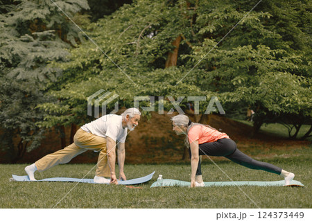 Senior man and woman with yoga mats standing at park. Positive mature man and his elderly wife have a fitness or yoga class in nature. Wellness and healthy lifestyle on retirement. 124373449