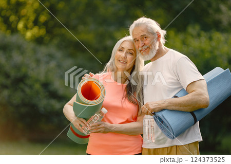 Senior man and woman with yoga mats standing at park. Positive mature man and his elderly wife after fitness or yoga class in nature. Wellness and healthy lifestyle on retirement. Senior man and woman with yoga mats standing at park. Positive mature man and his elderly wife after fitness or yoga class in nature. Wellness and healthy lifestyle on retirement. 124373525