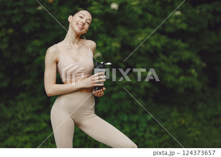 Pretty lady training in a summer park. Brunette doing yoga. Girl in a sportsuit. 124373657