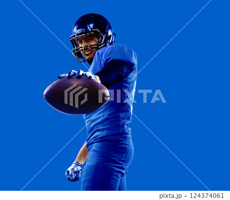 Energetic collage. Powerful american football player extending arm with ball, dressed in blue, matching intense monochrome background. 124374061