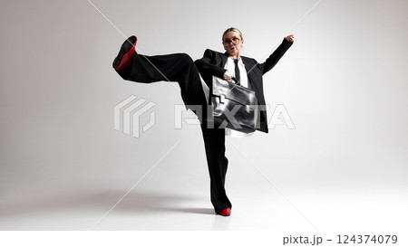 Full-length dynamic image of young woman, employee, dressed stylish black attire, stand with raised leg, ready to fight with challenges against white background. 124374079