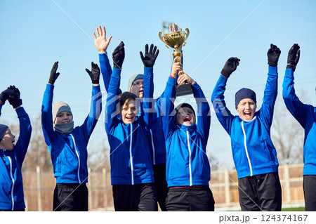 Champions Moment. Youth soccer players lifting golden trophy, cheering with excitement and pride. Pure happiness. 124374167