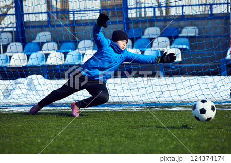 Diving for Victory. Young goalkeeper stretching mid-air to prevent goal, showcasing determination and commitment to defending net. Diving for Victory. Young goalkeeper stretching mid-air to prevent goal, showcasing determination and commitment to defending net. 124374174