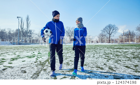 Two young football players in blue uniforms walking on snowy field, bonding during practice session. Concept of sport, school. 124374198