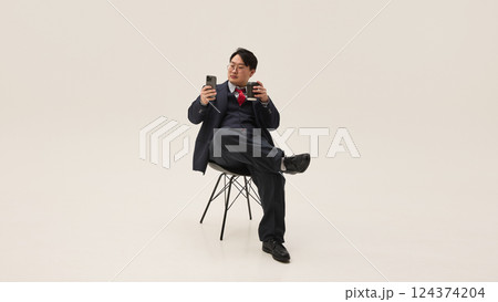 Coffee break. Young Asian man browsing on phone and drinking coffee having rest time against white background. Coffee break. Young Asian man browsing on phone and drinking coffee having rest time against white background. 124374204