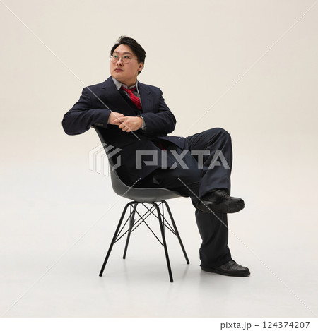 Businessman, Asian guy, dressed formal attire looking away, sitting on chair and exuding confidence and focus against white background. Businessman, Asian guy, dressed formal attire looking away, sitting on chair and exuding confidence and focus against white background. 124374207