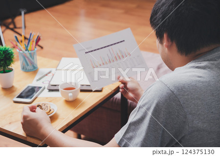 A man in casual wear picks up cookies while he is working at home office. 124375130
