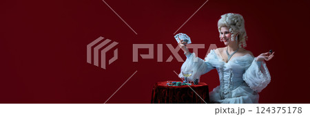 Confident winner. Stylish rococo woman with cards and chips, posing like casino queen in white baroque gown. 124375178