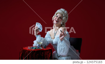 Joyful game. Medieval female character laughing while playing poker, surrounded by chips and wine. 124375183