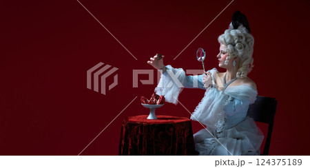 Gem analysis. Noble woman in elegant white dress using magnifier to inspect ruby ring over pomegranate Gem analysis. Noble woman in elegant white dress using magnifier to inspect ruby ring over pomegranate 124375189