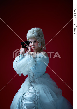 Mysterious beauty. Baroque-styled woman lifting black mask to face with confident gaze in elegant vintage dress. 124375199