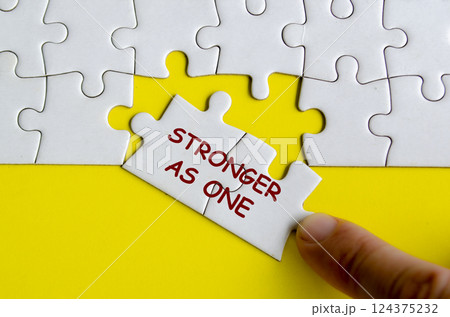Hand putting missing jigsaw puzzle with text saying Stronger As One. Unity and Teamwork concept 124375232