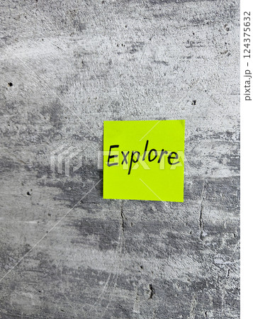 Bright yellow sticky note with the word Explore prominently displayed on a textured grey background, signifying the spirit of adventure and the pursuit of new experiences 124375632