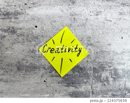 Vibrant yellow sticky note shaped as a diamond displaying the word Creativity and decorative elements on a textured grey background, representing the essence of innovative thinking and inspiration 124375639