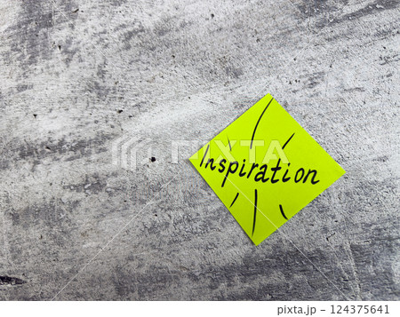 Vibrant yellow sticky note in a diamond shape displaying the word Inspiration with decorative elements on textured grey surface, representing the essence of motivating ideas and creative potential 124375641