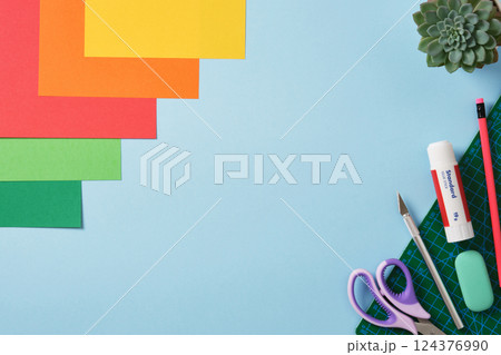 Supplies for paper art hobby: scissors, craft knife, pencil, eraser, colored paper. Space for your text. Paper crafts work table flatlay. 124376990