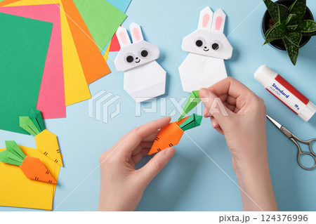 Women's hands make paper origami carrot. Around paper crafting tools. DIY project concept for children, hobby and creativity. 124376996