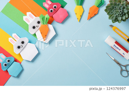 Frame made of paper crafting tools: scissors, cutter, glue and colored paper. Origami rabbits and carrots. DIY concept, needlework. Flat layer, copy space 124376997