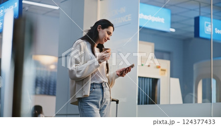 Busy Airport Terminal: Adult Woman Scrolling on Smartphone, Drinking Coffee, Waiting for Flight 124377433