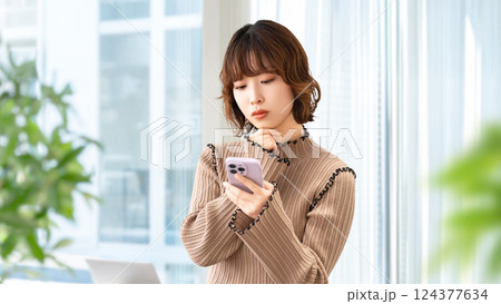 スマートフォンを見て考える女性・ビジネスウーマン スマートフォンを見て考える女性・ビジネスウーマン 124377634