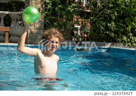 Teenager plays ball and swims in swimming pool in summer. Eleven years year old boy playing in pool with ball. Outdoors. Summer vacation Teenager plays ball and swims in swimming pool in summer. Eleven years year old boy playing in pool with ball. Outdoors. Summer vacation 124378427