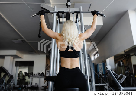 Athletic woman exercising back muscles using lat machine in gym 124379041