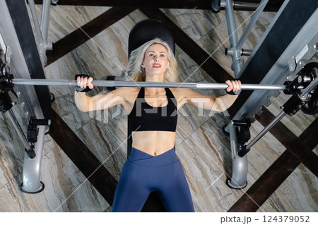 Determined sportswoman lifting barbell while exercising on bench press in gym Determined sportswoman lifting barbell while exercising on bench press in gym 124379052