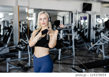 Fitness instructor wearing headphones and gloves pointing in the gym Fitness instructor wearing headphones and gloves pointing in the gym 124379054
