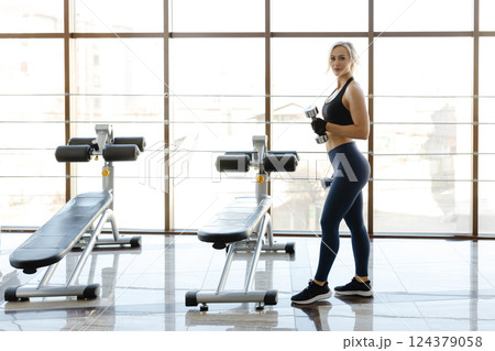 Determined sportswoman lifting dumbbells in a gym with natural light 124379058