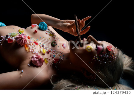 Woman with body art and colorful sweets lying on a dark surface 124379430